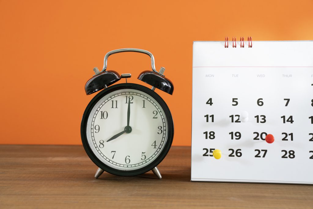Retro alarm clock and calendar on wooden table with orange background