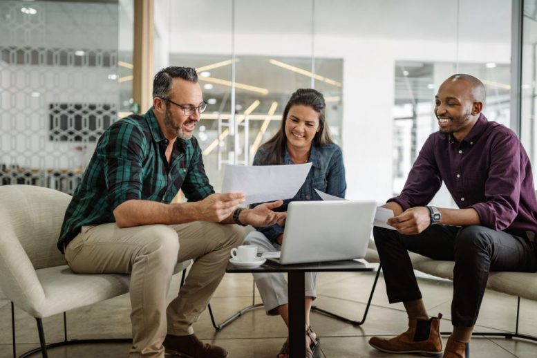 Three smiling diverse business colleagues having casual sit down business strategy meeting.