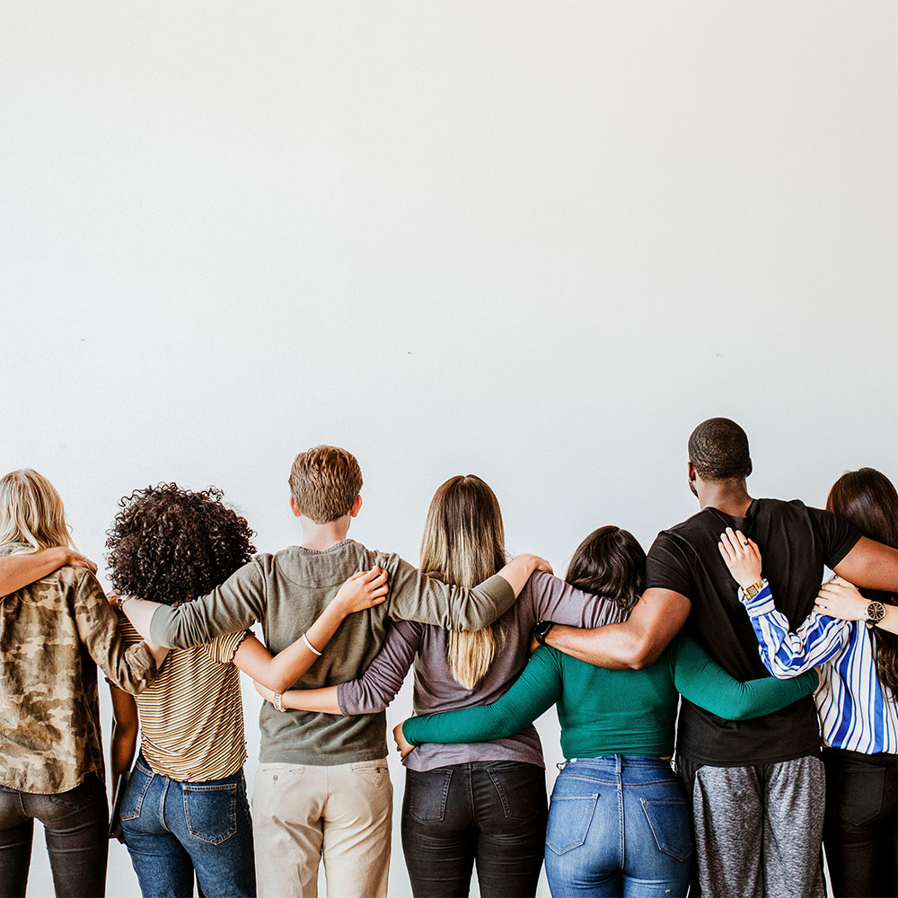 Seven adults standing shoulder to shoulder with arms embracing each other