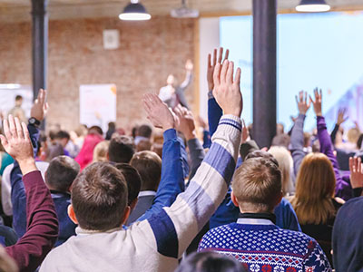 Large audience of adults sitting facing stage with hands raised