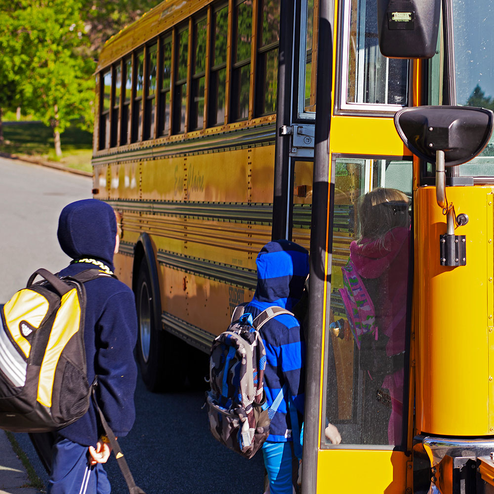 Two children wearing backpacks getting onto a school bus