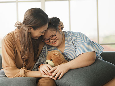 Mother and daughter sitting on couch smiling and hugging