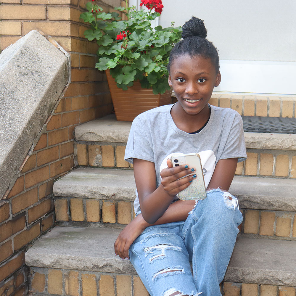 Girl smiling and sitting on step with smart phone in her hand