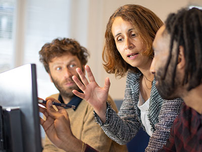 Teacher assisting two adults at computer