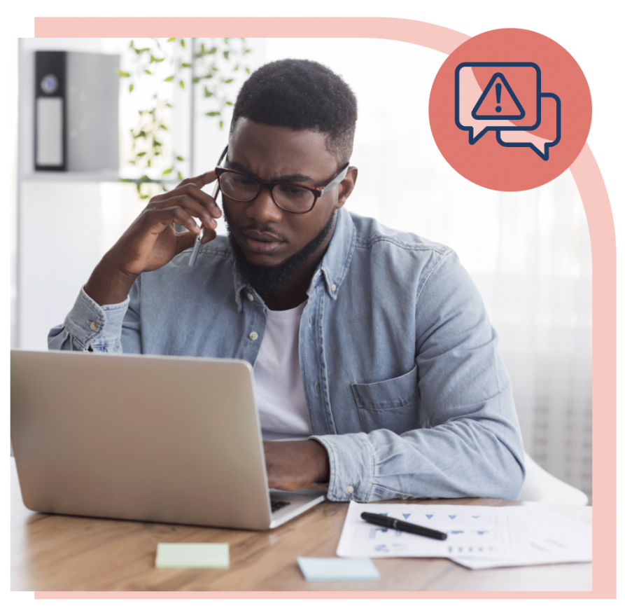 Man wearing glasses with a serious expression looking at his laptop and talking on his smartphone