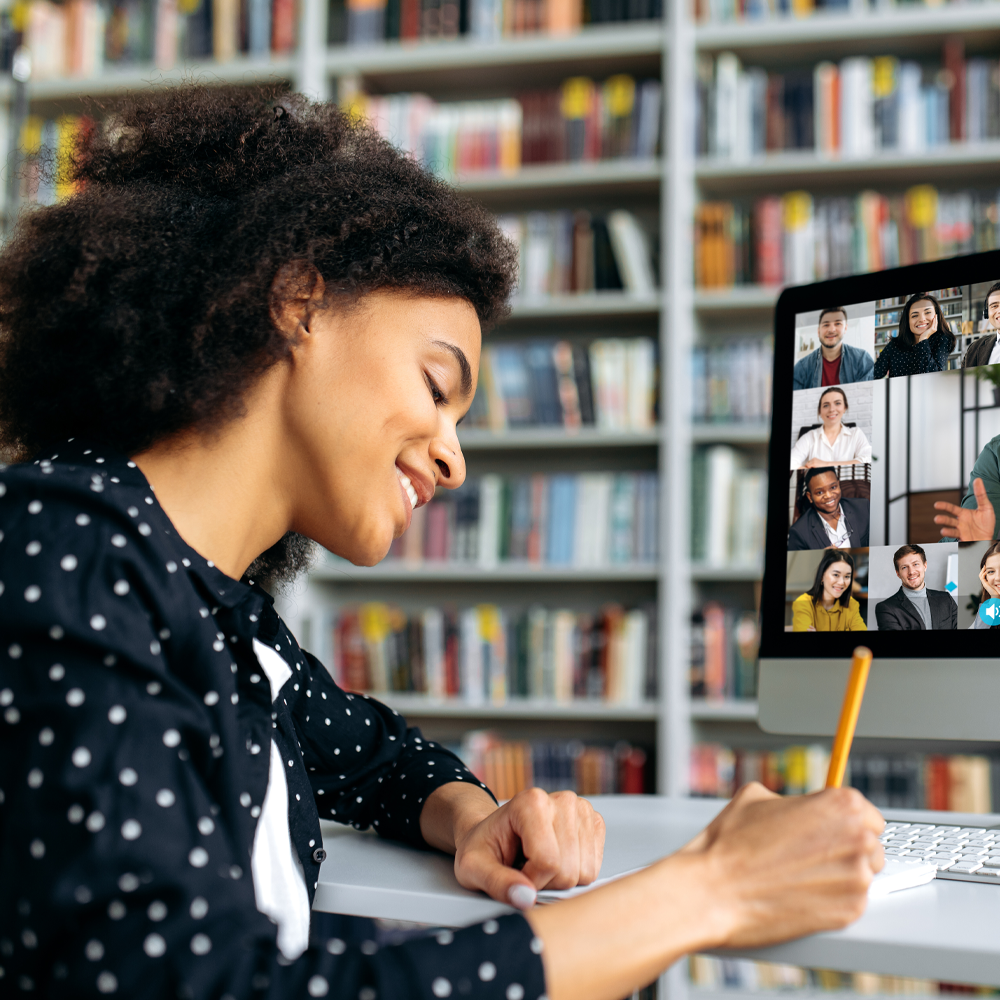 Woman writing down notes while on a large video call on a desktop computer