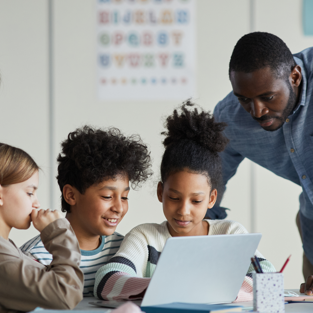 Teacher helping three young students working on a laptop