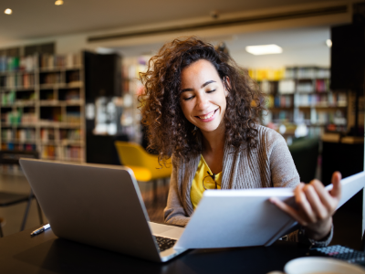 Woman happily looking at her notebook in front of her laptop in a library