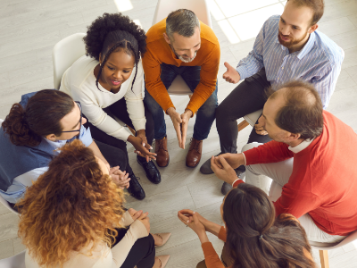 Diverse group of adults sitting in chairs arranged in a circle, huddled together and having a discussion
