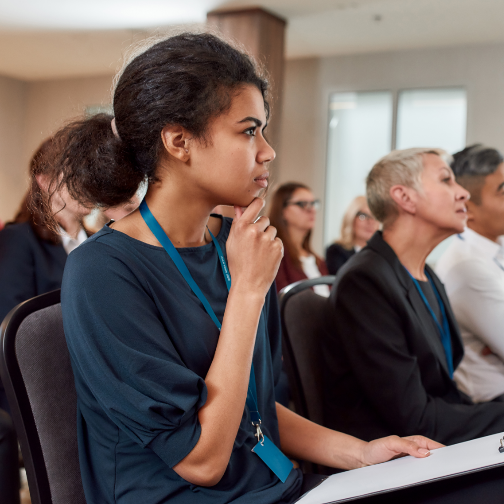 Diverse audience in a business seminar with a focus on a young woman deep in thought with a clipboard in her hand