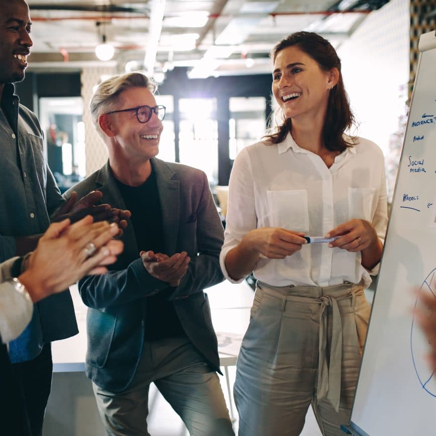 Small diverse group of adults clapping at woman's whiteboard presentation