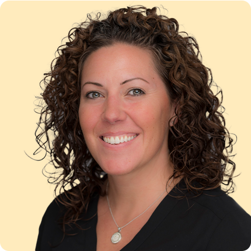 A woman with shoulder length dark curly hair is looking at the camera and smiling
